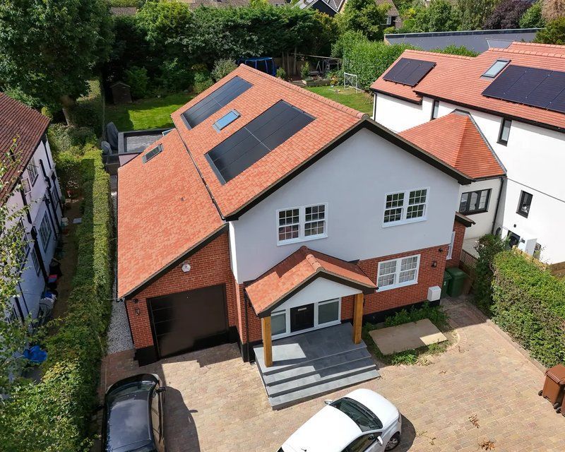 An aerial view of a two-story house with a red tile roof, solar panels, and a white and red brick facade.