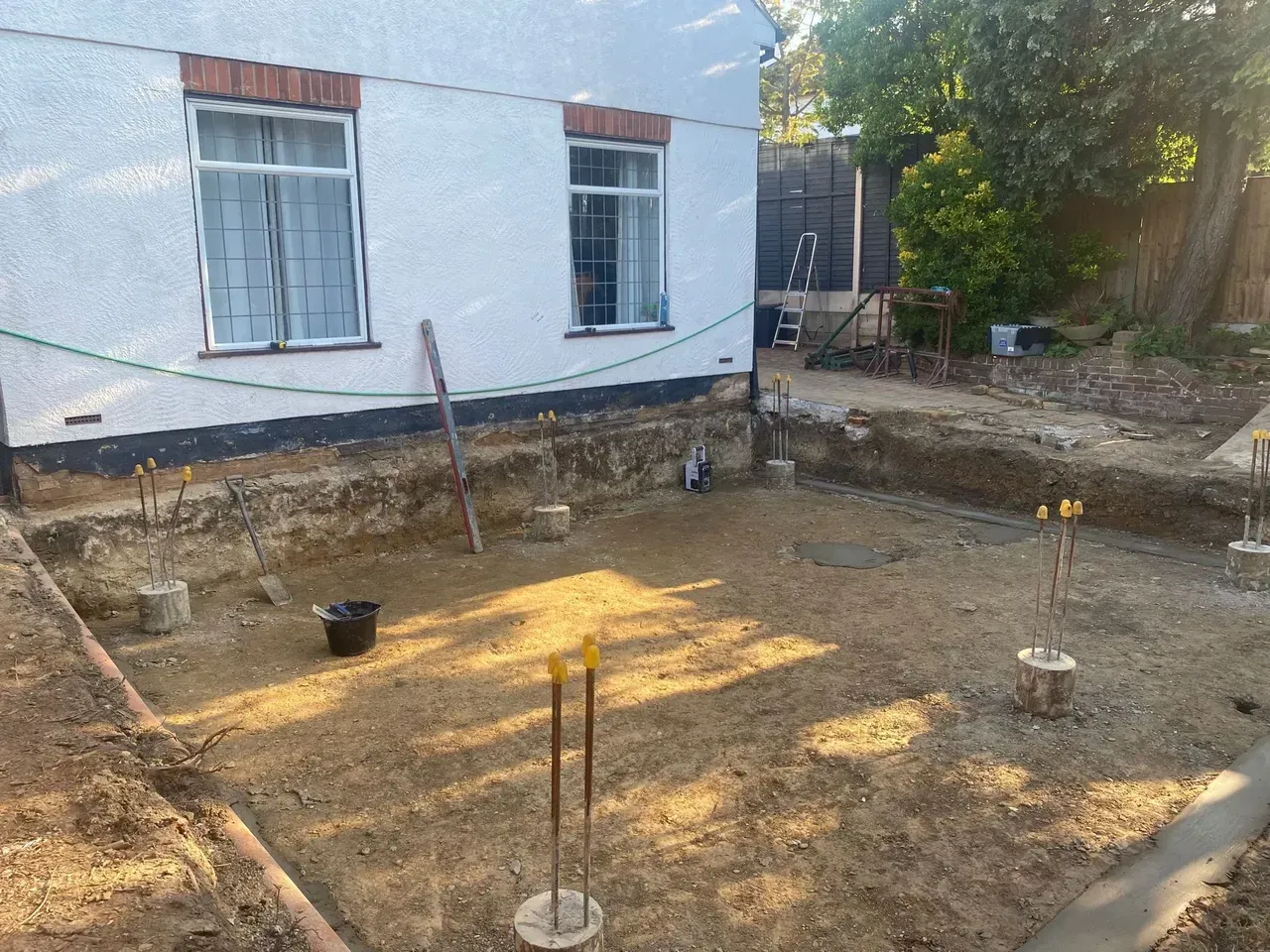 Construction site: foundation dug with concrete footings. Building in background.