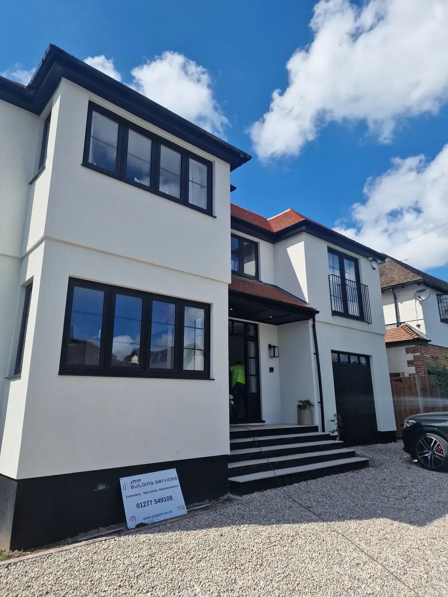 White house with black trim, windows, and garage door under a blue sky with fluffy clouds.