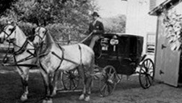 A man is riding a horse drawn carriage in a black and white photo.