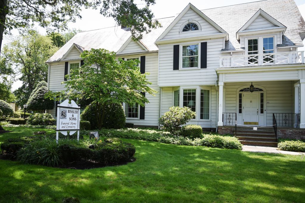A large white house with black shutters and a sign in front of it