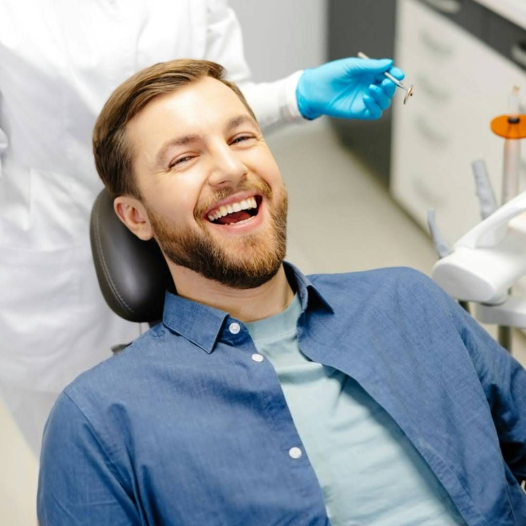 A laughing person sitting in a dental chair with a dentist in blue gloves standing behind them.