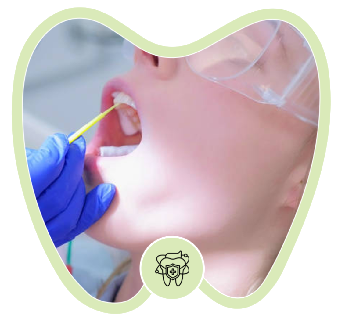 A gloved hand uses a small applicator to apply treatment to a patient's teeth in a dental office.