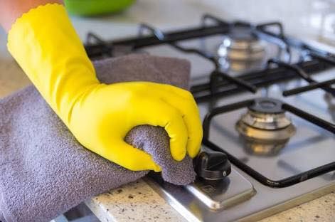 Someone Wiping Kitchen Stove with Cloth and Yellow Gloves — Carpet Cleaners in Tatura, VIC