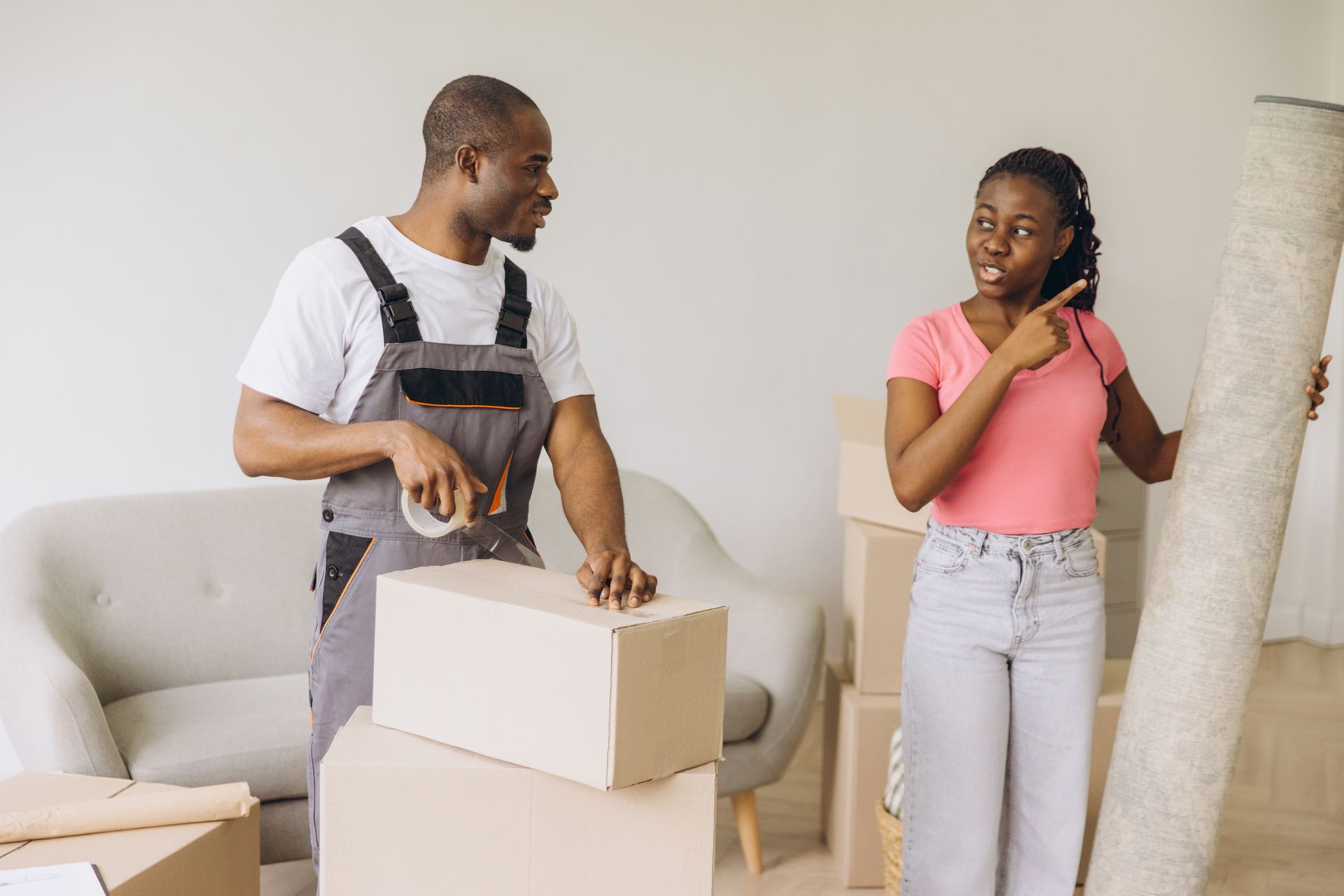 An African American mover packing next to a female African American client carrying a rolled carpet.