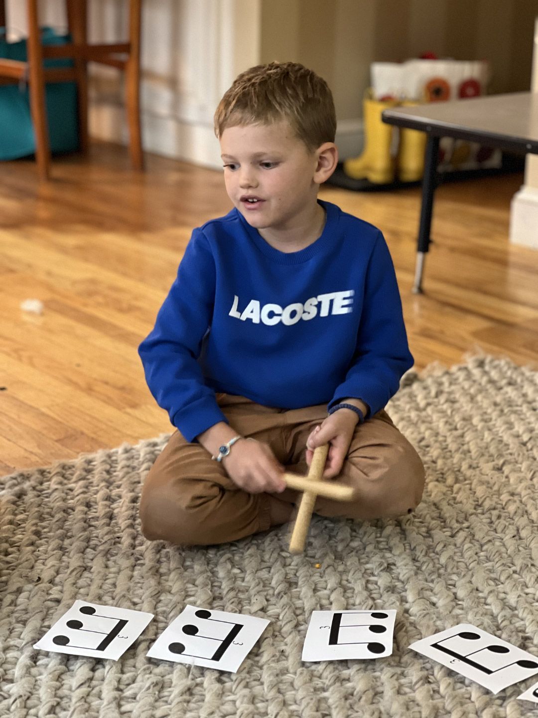 A primary Montessori child uses rhythm sticks to follow musical notation cards during a classroom music lesson.