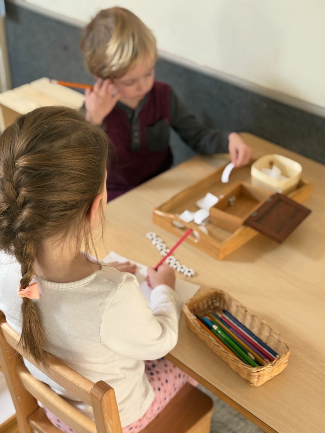 Primary Montessori children work at a table practicing writing and language skills with paper and colored pencils.