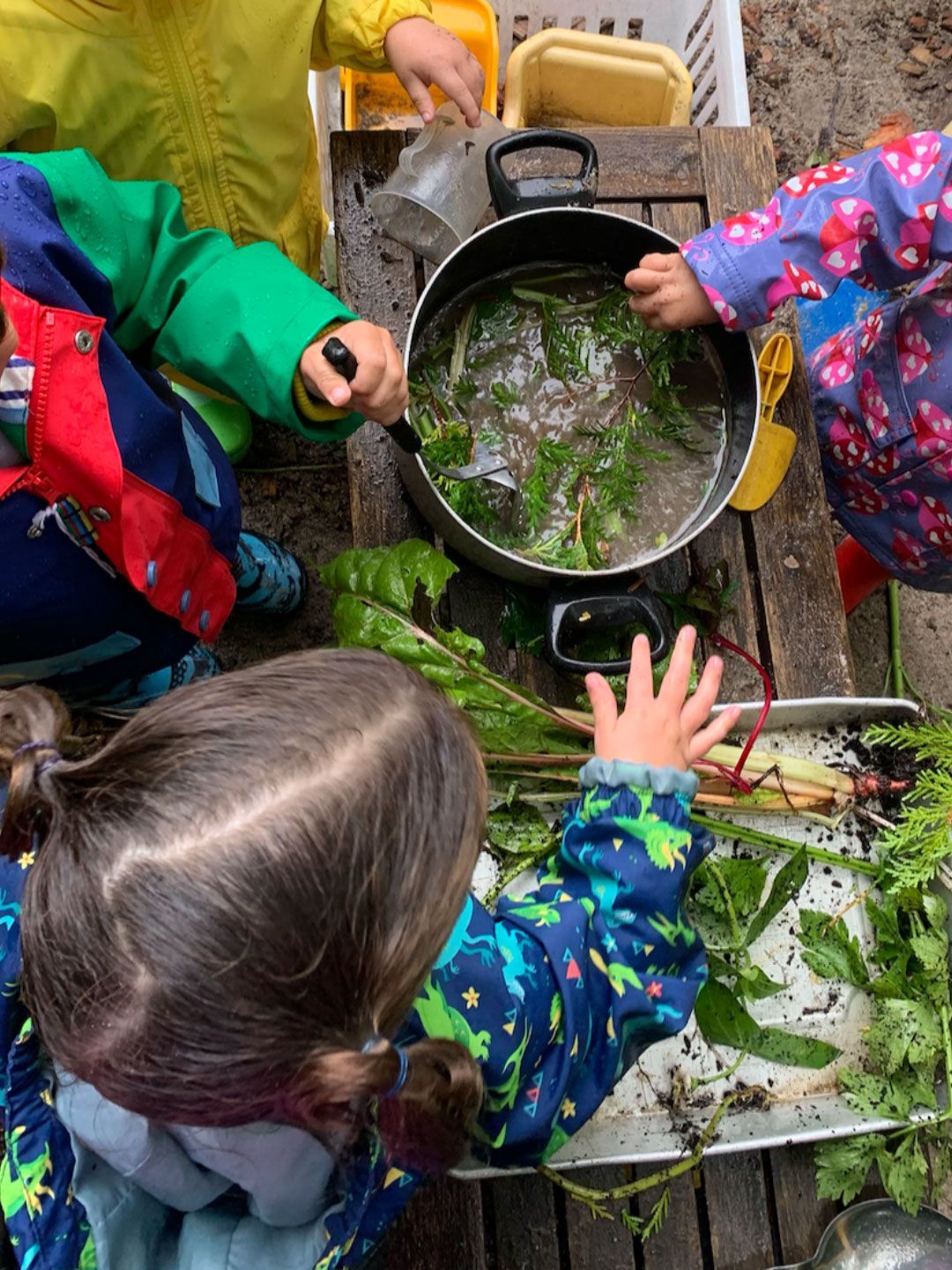 Toddler Montessori children engage in sensory outdoor play and practical life at a mud kitchen.