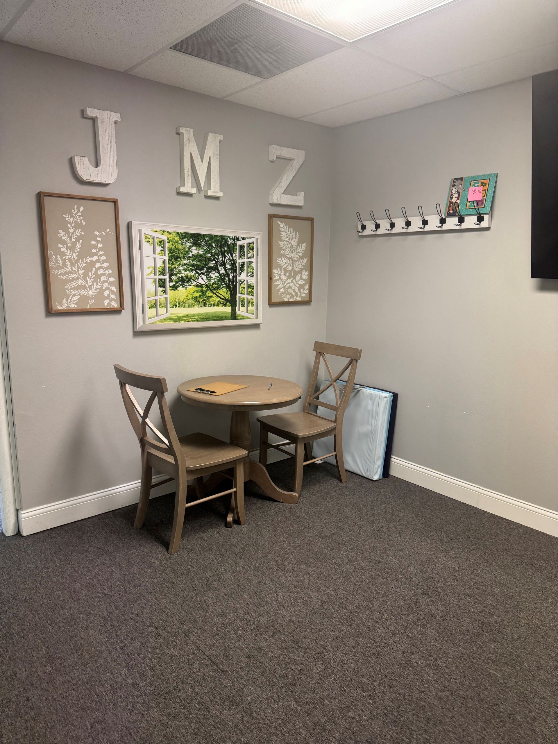 Cozy office corner with a small table and chairs, art, and wall decor, on gray carpet.