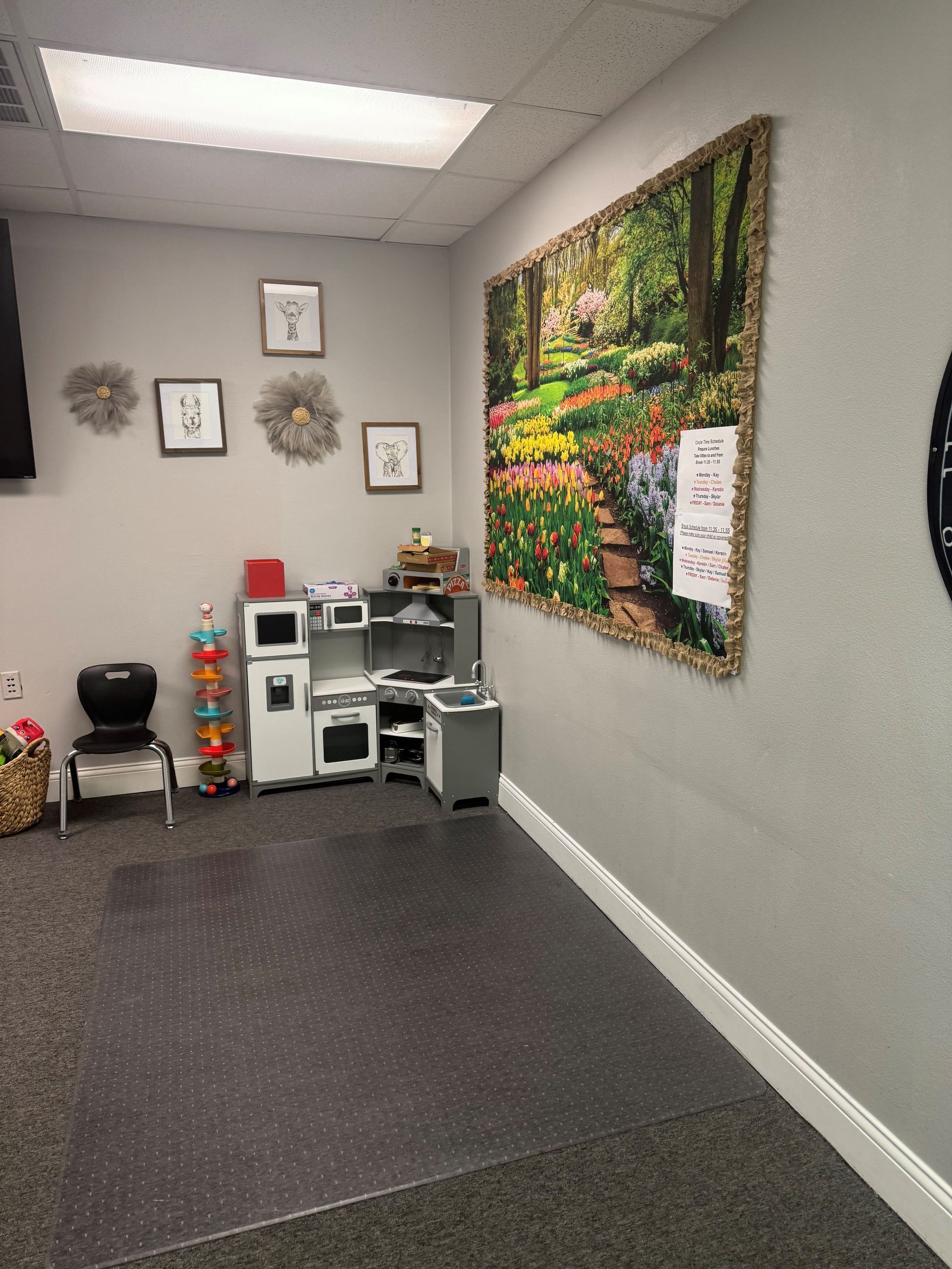 Play area with child-sized kitchen, artwork, and toys in a room with gray walls and a dark floor.