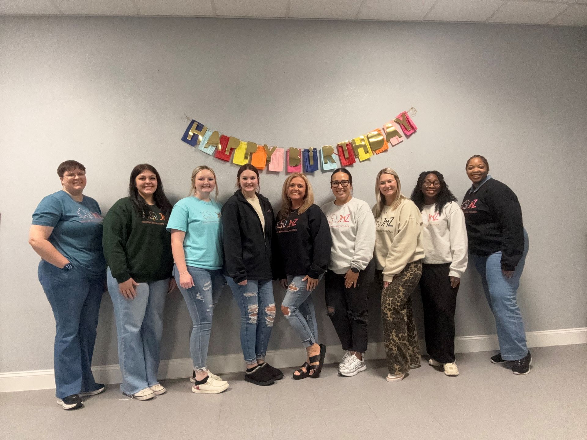 Group of nine women stand in front of a banner. They are smiling and wearing casual clothes.