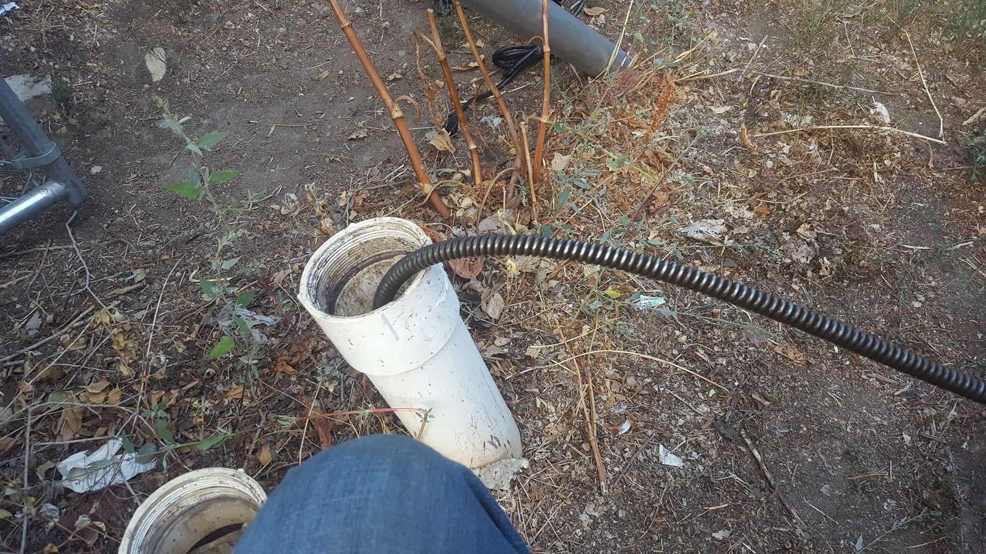 A person is sitting on the ground next to a pipe with a hose attached to it.