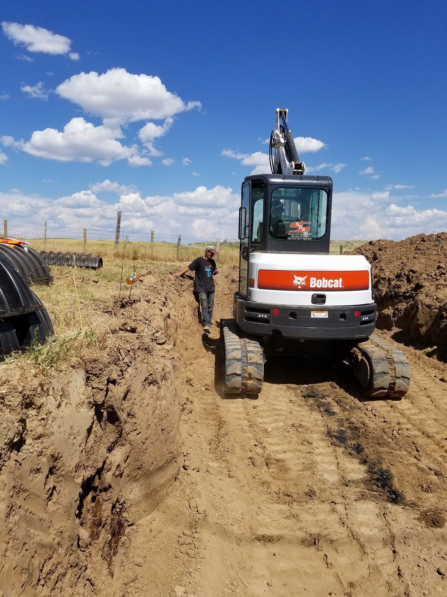 A man is walking next to a bobcat excavator on a dirt road.