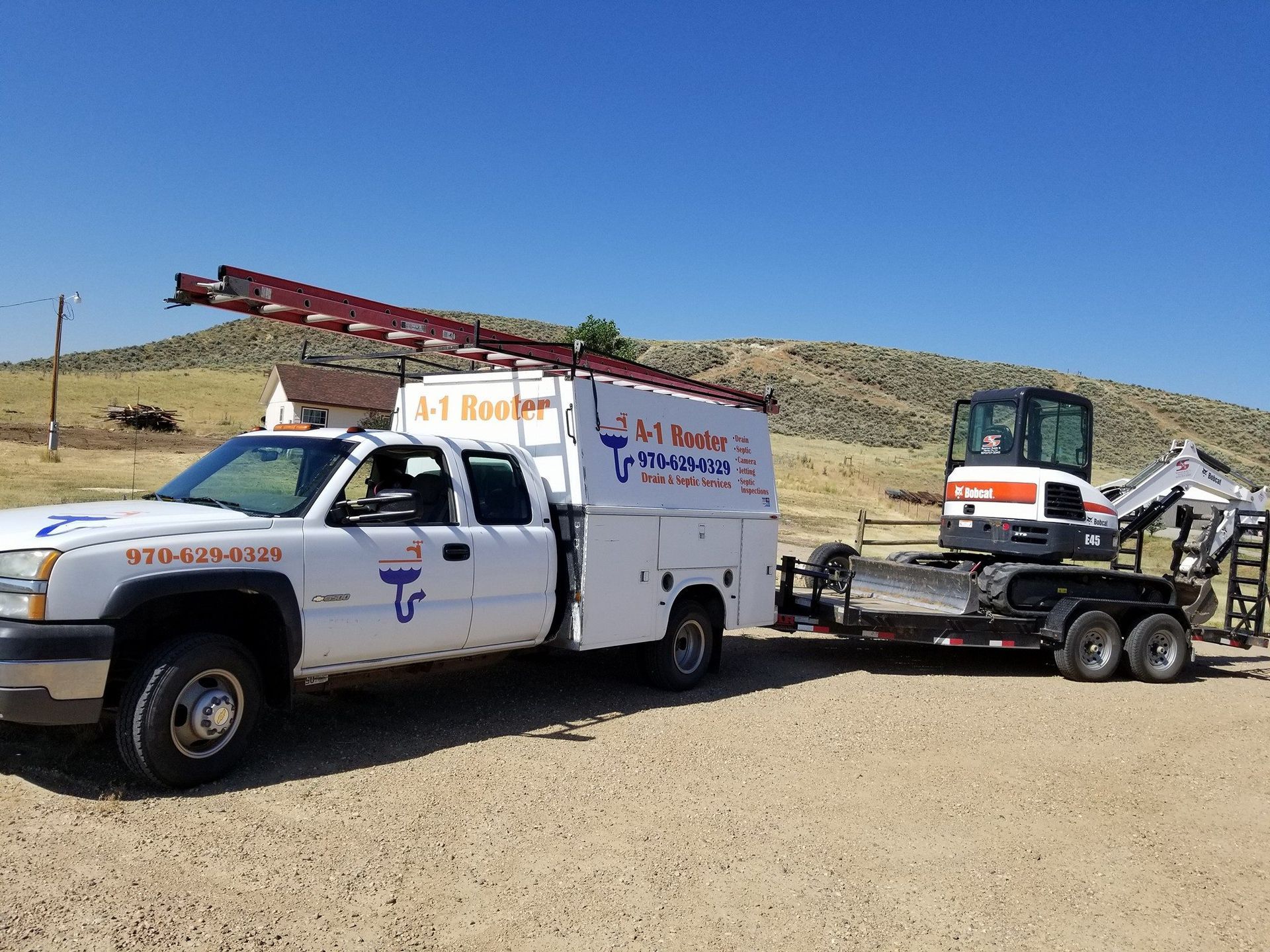 A white truck with a ladder on top of it is parked next to an excavator on a trailer