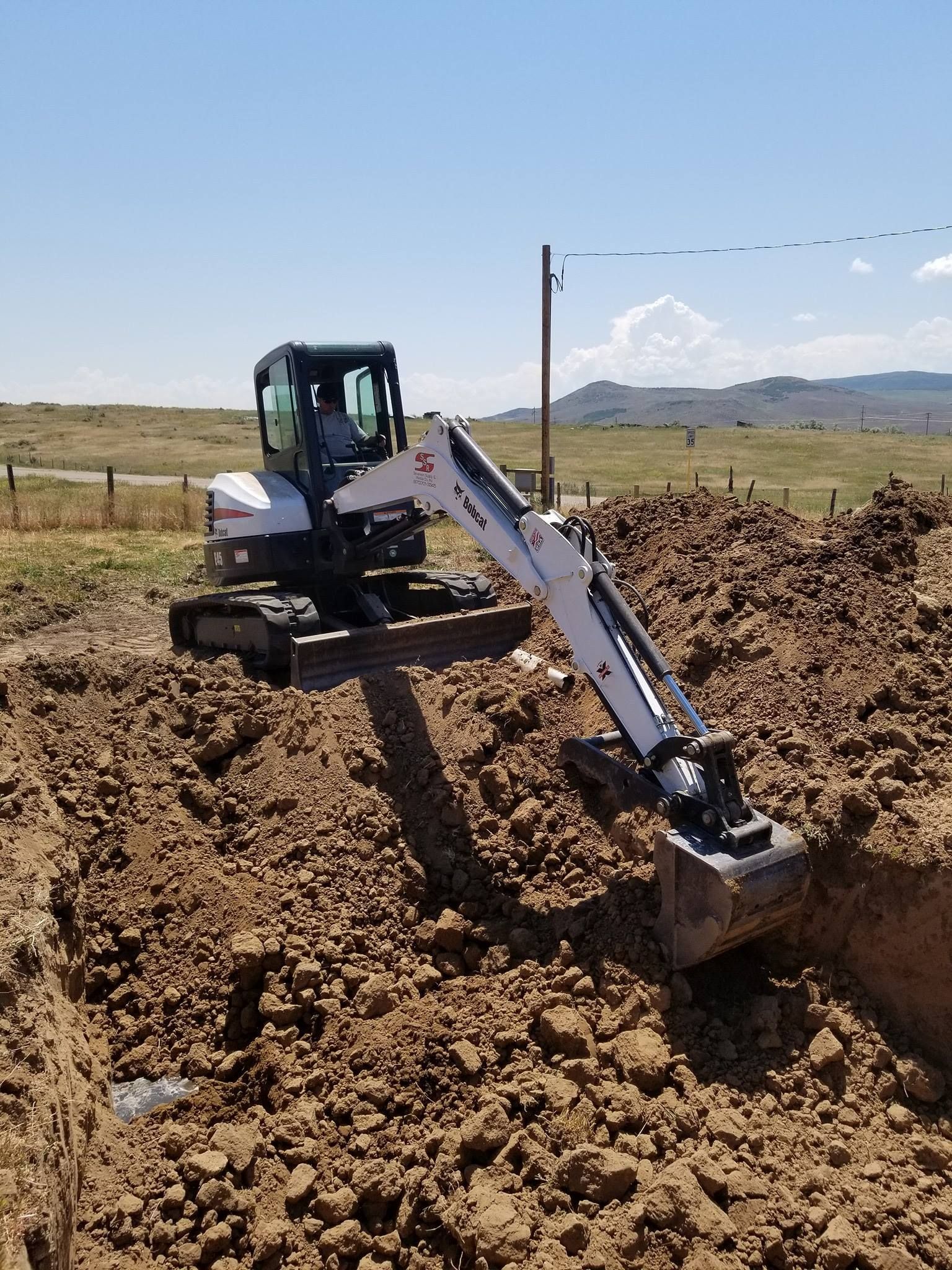 A small excavator is digging a hole in the dirt in a field.
