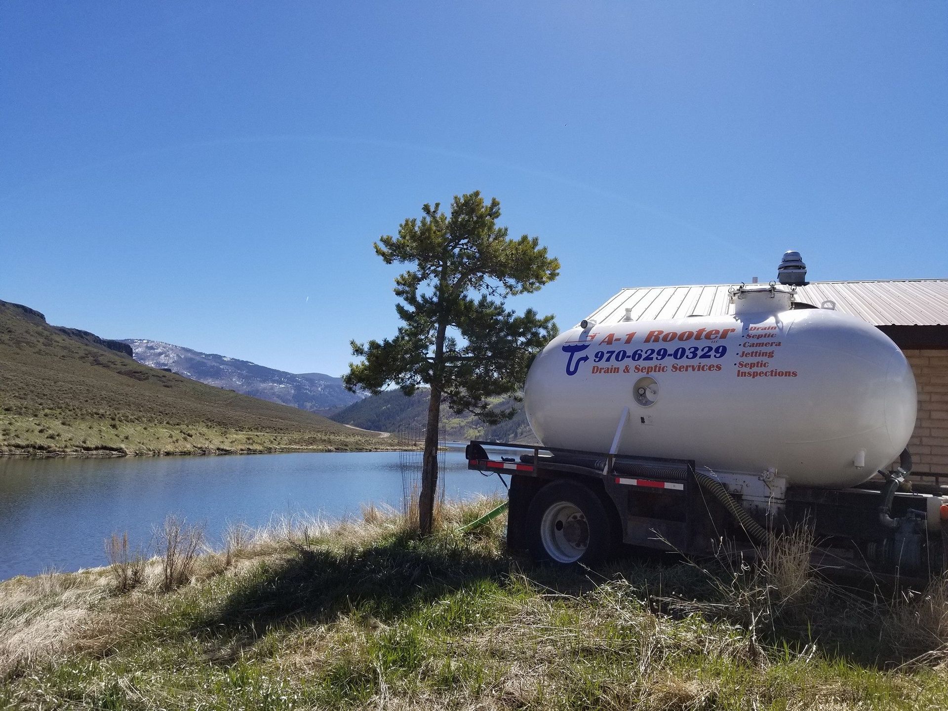 A tanker truck is parked near a lake with mountains in the background