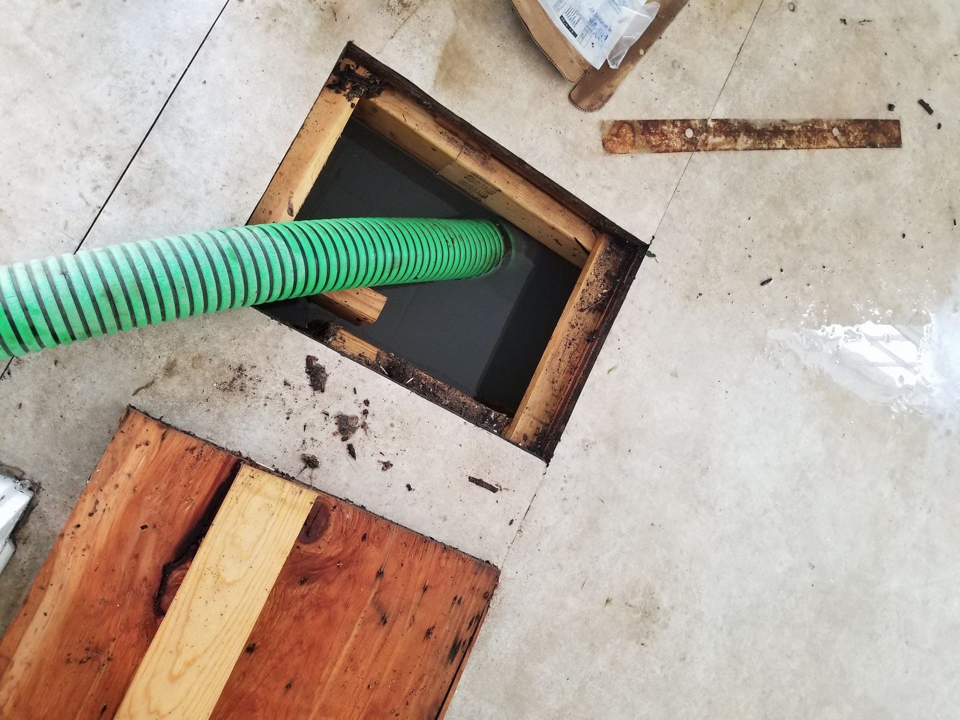 A green hose is being used to pump water into a hole in the floor.