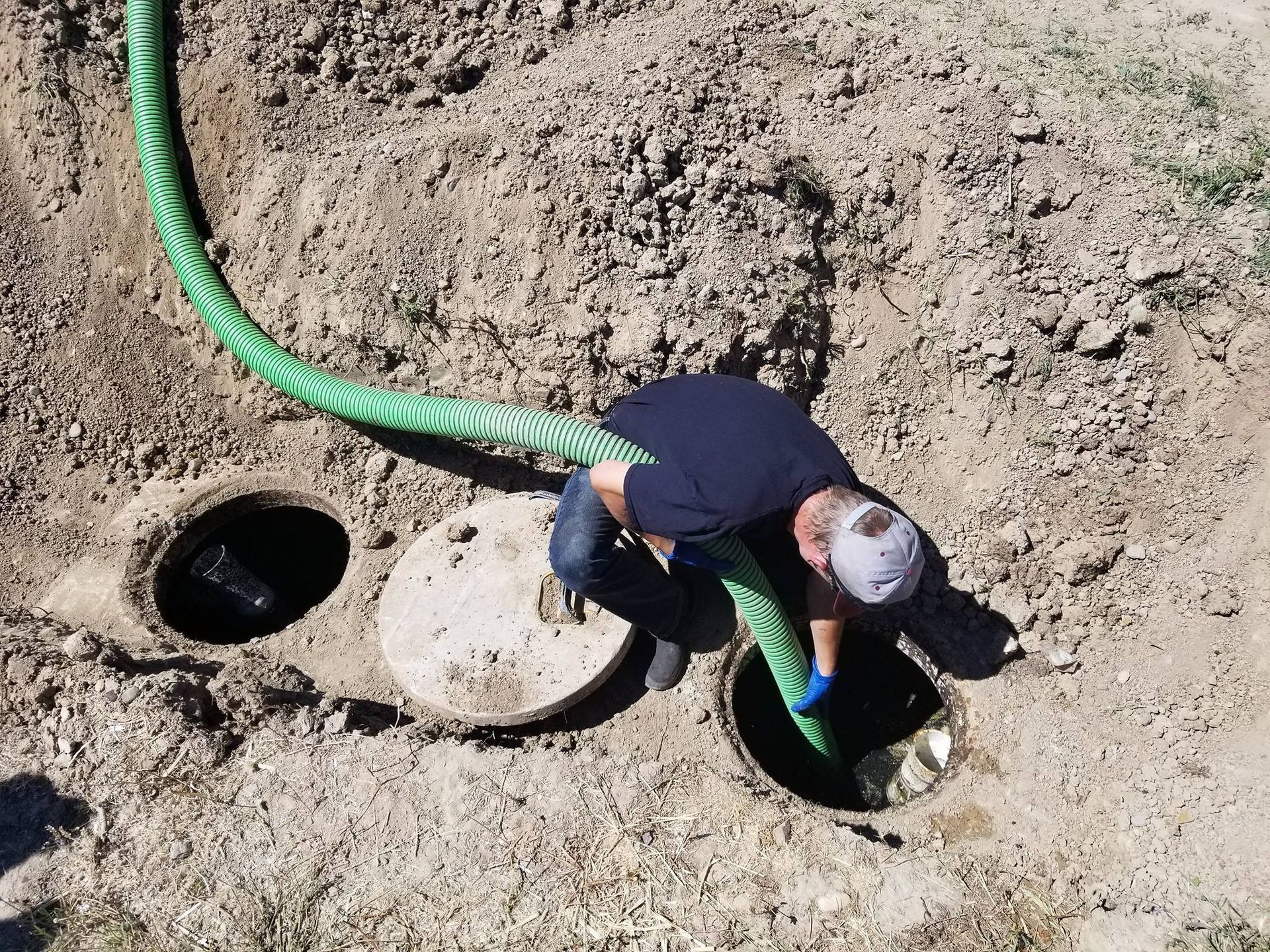 A man is using a green hose to pump water into a septic tank.