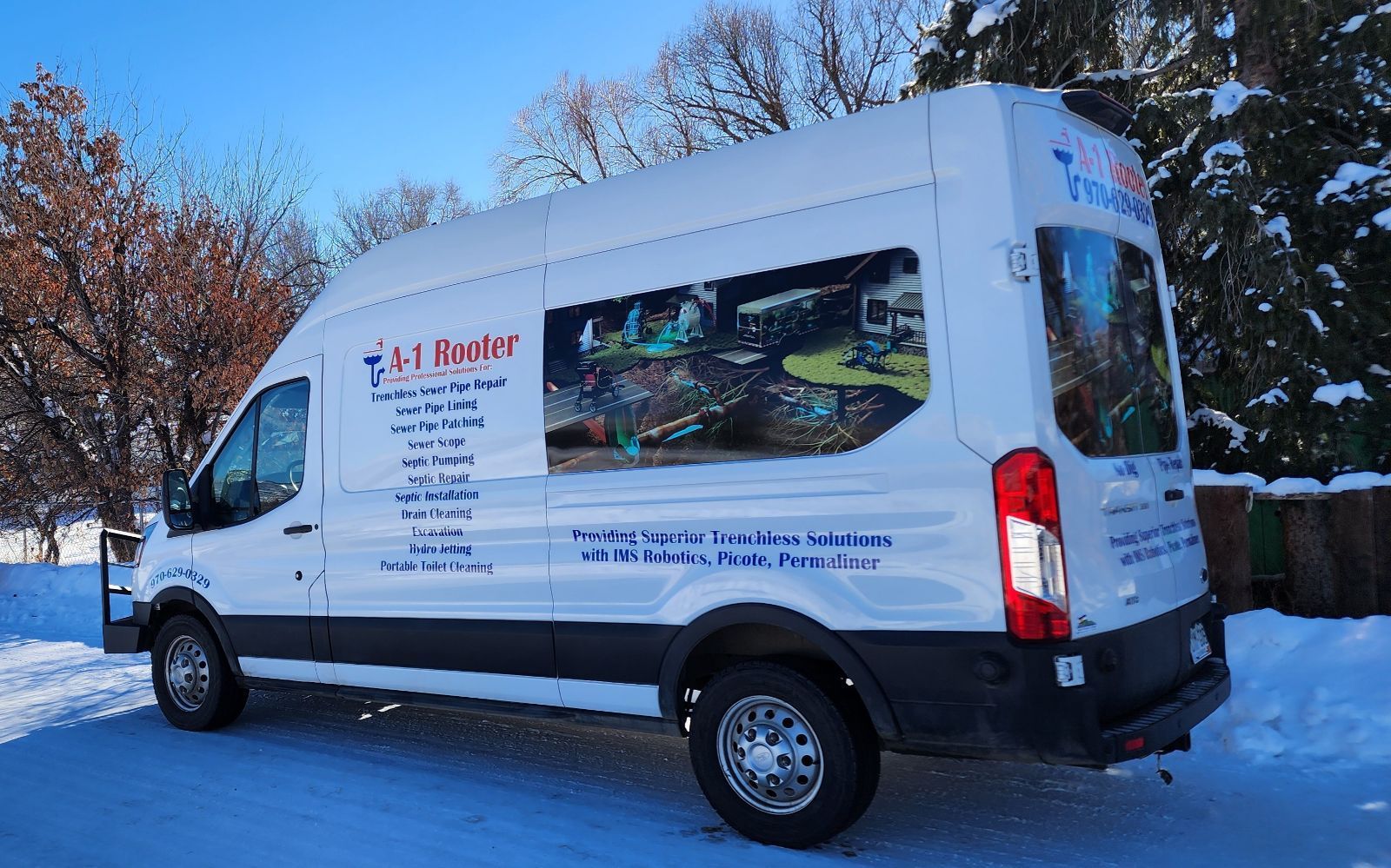 A white van is parked in the snow with trees in the background.