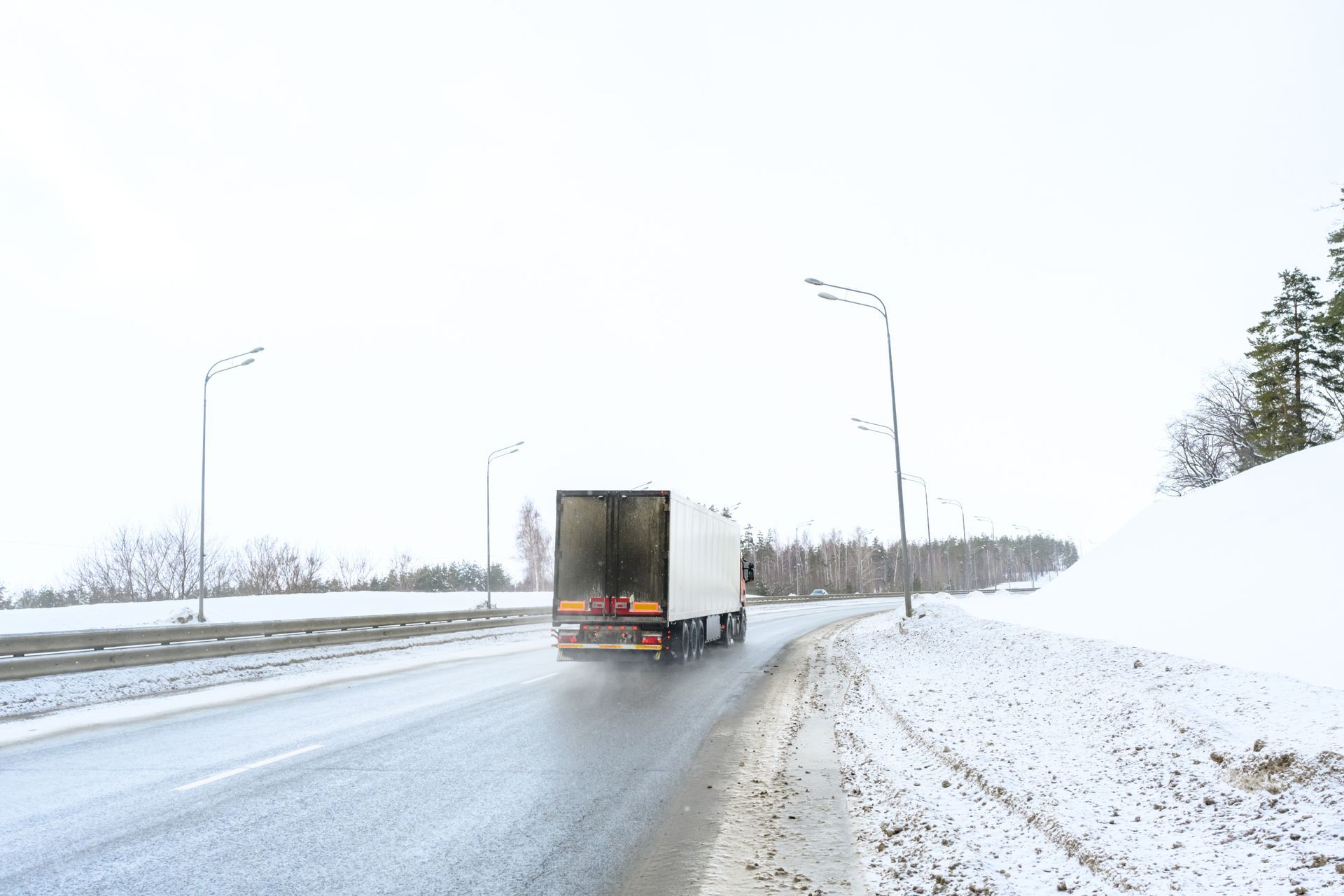 Semi-truck driving on a wet road, snowy landscape, overcast sky.