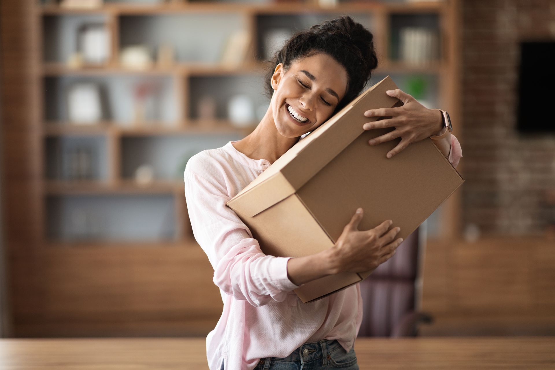 a woman in a pink shirt is hugging a cardboard box