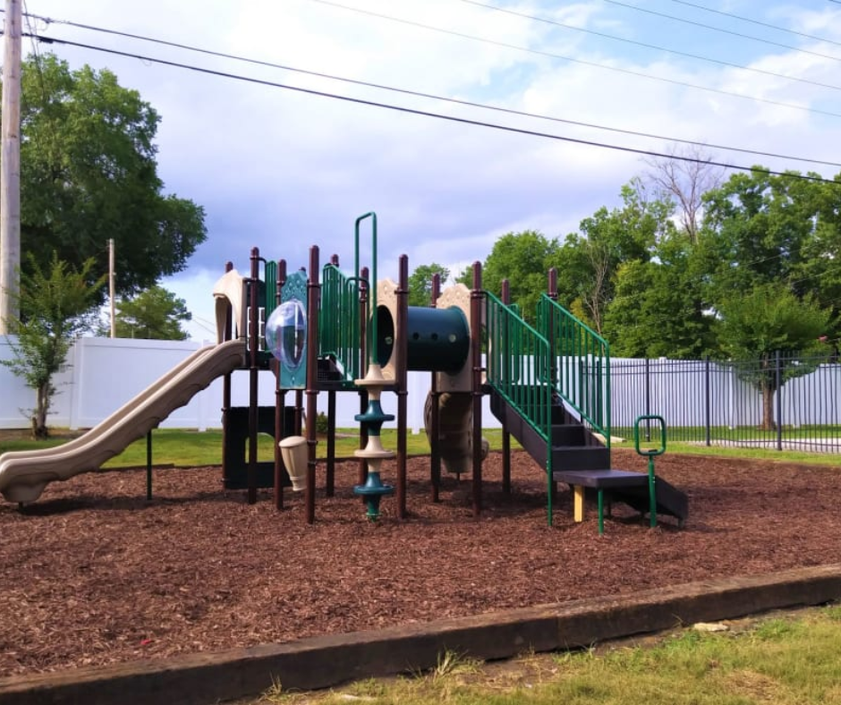 A playground set with a slide, tunnel, and stairs, situated on wood mulch in a yard enclosed by a fence.