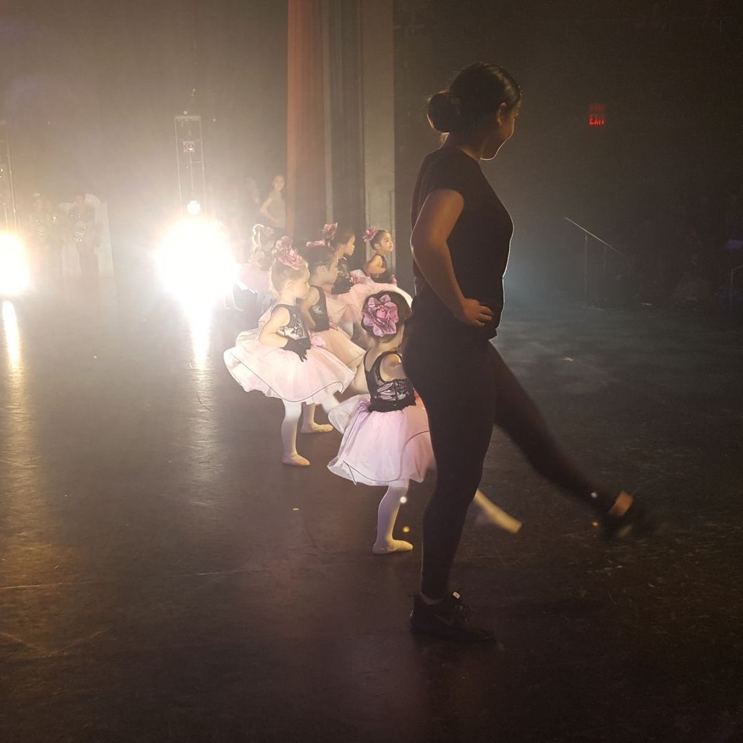 A woman is walking on a stage next to a group of dancers.