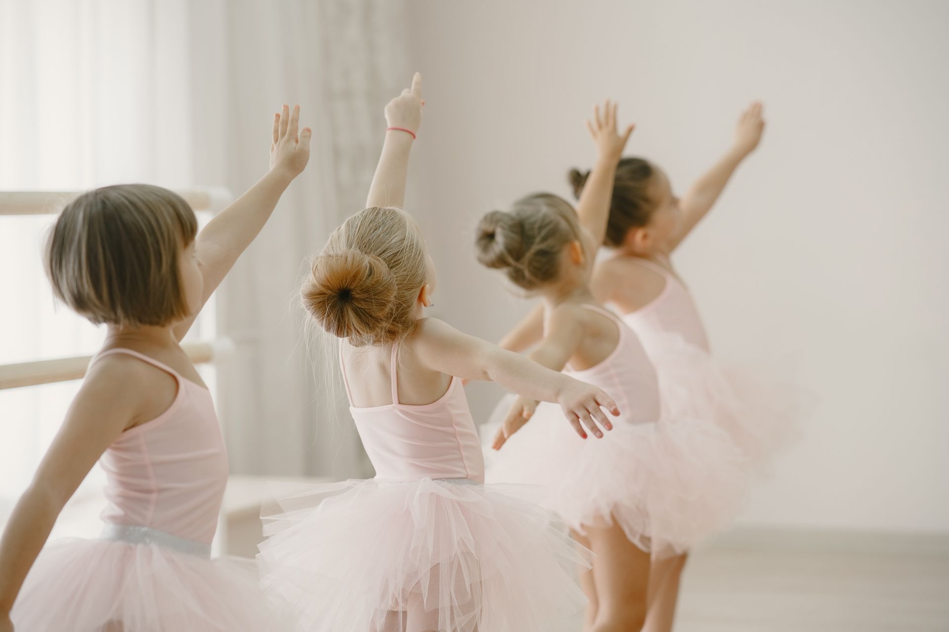A group of young girls in pink tutus are dancing in a dance studio.