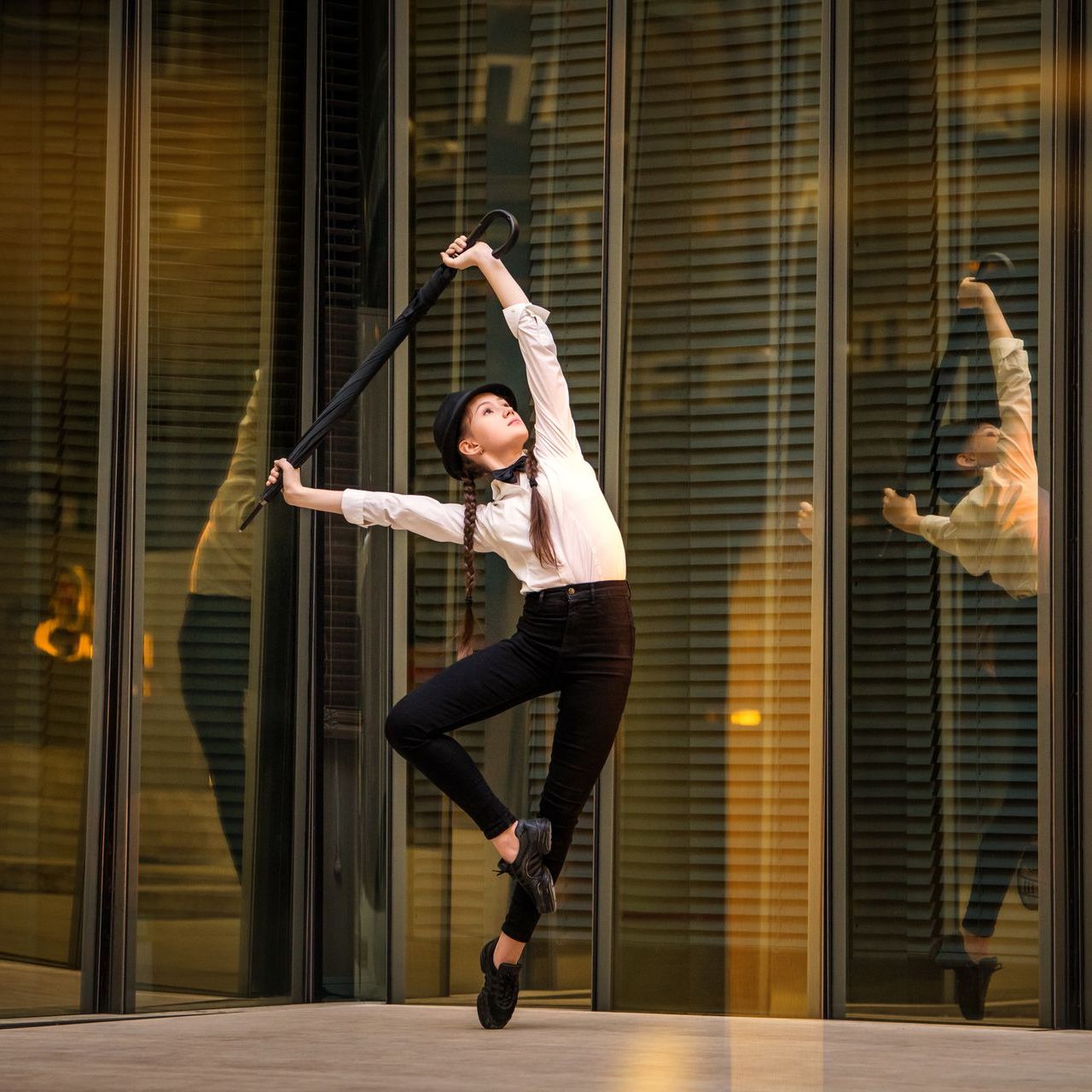 A woman is dancing in front of a glass building while holding an umbrella.