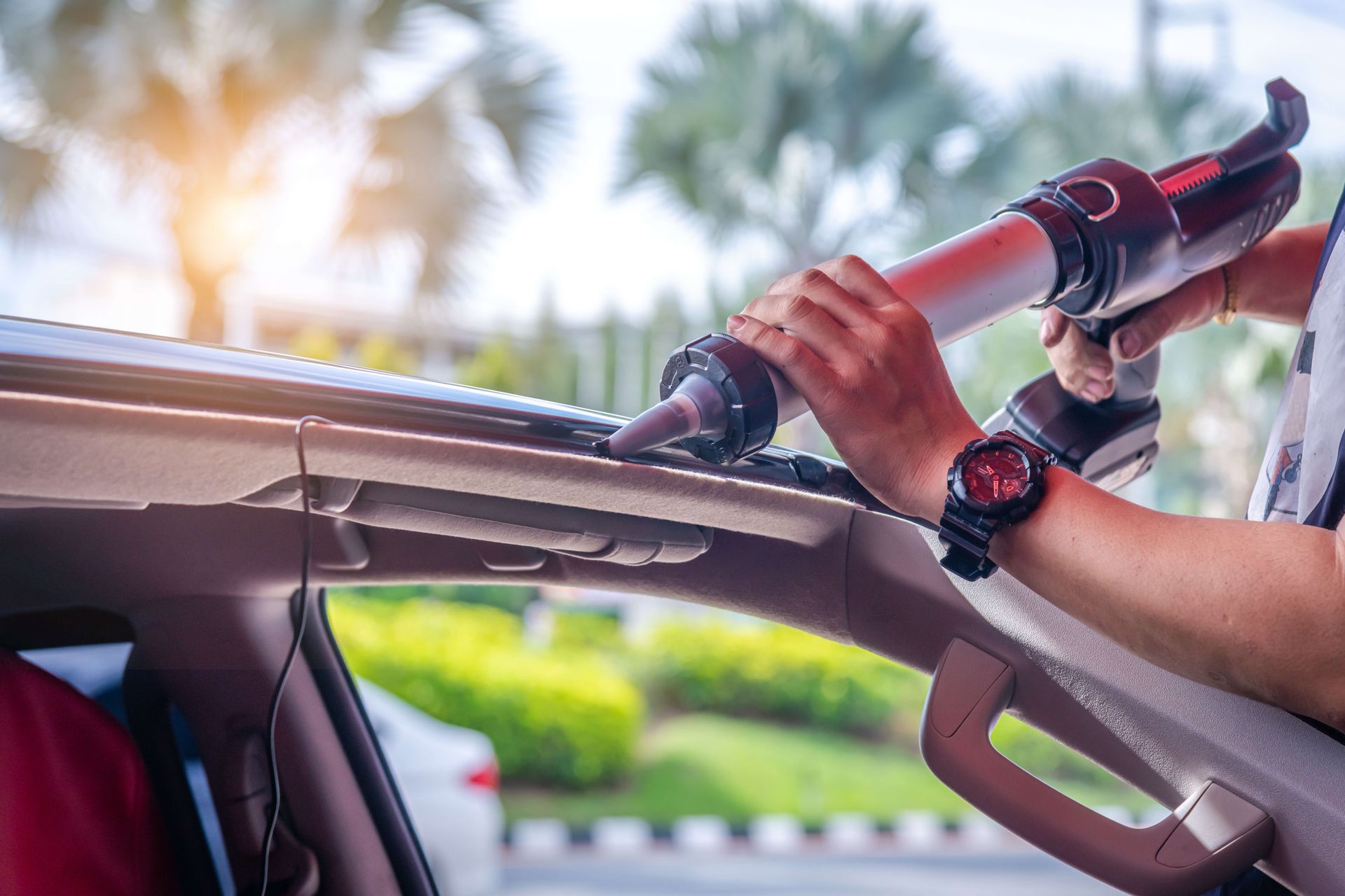 Person using a caulking gun on a car's roof, outdoors.