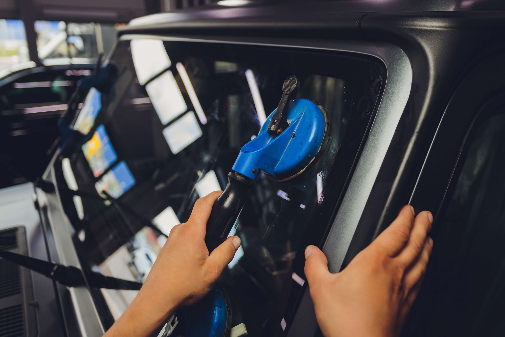 Hands using a blue suction cup tool to install car windshield glass.