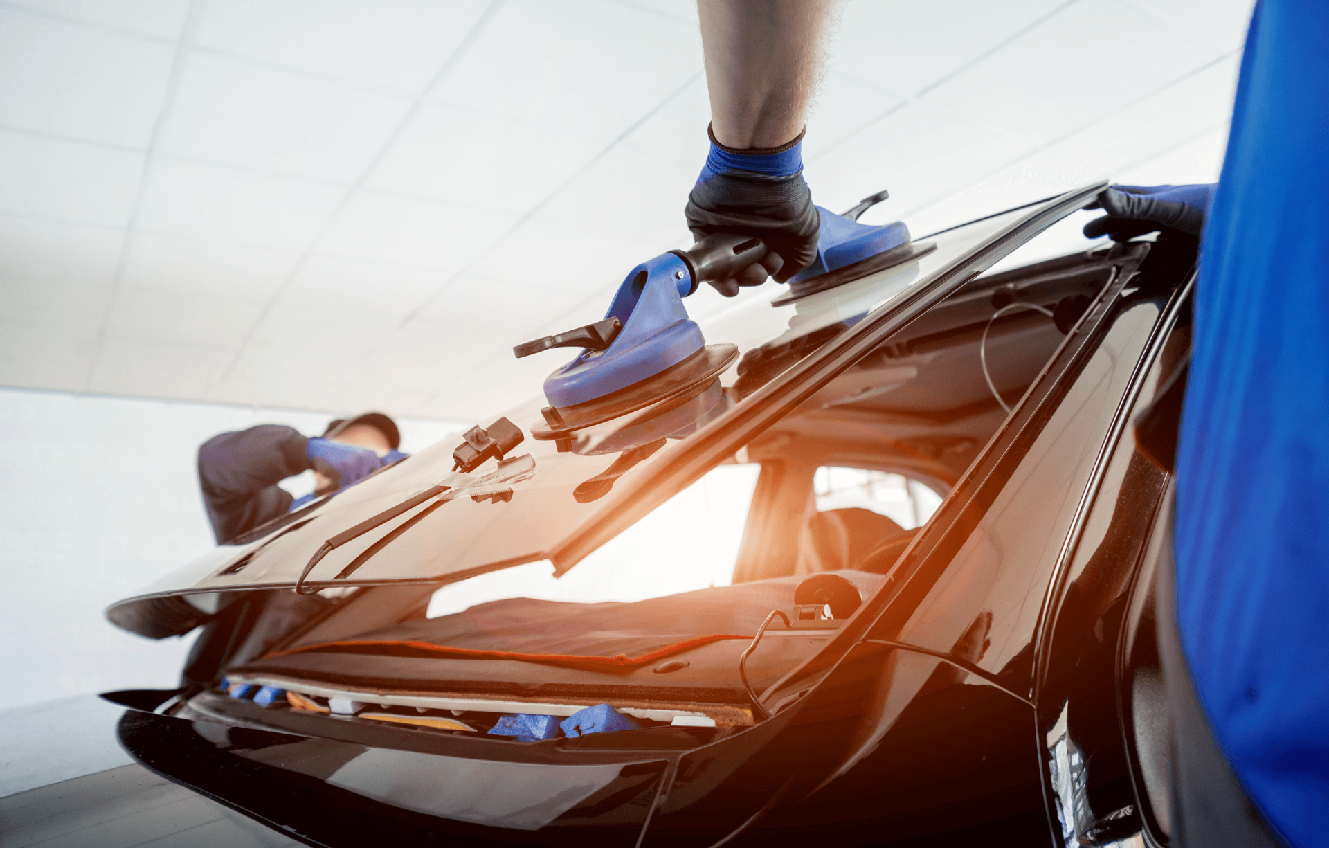 Two technicians installing a car windshield with suction cups.