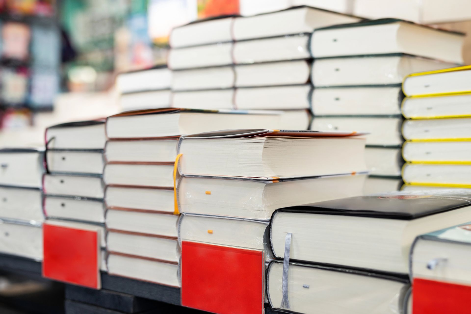 Pile di libri con copertina rigida disposte sugli scaffali, molti dei quali con piccole etichette rettangolari rosse sul dorso.