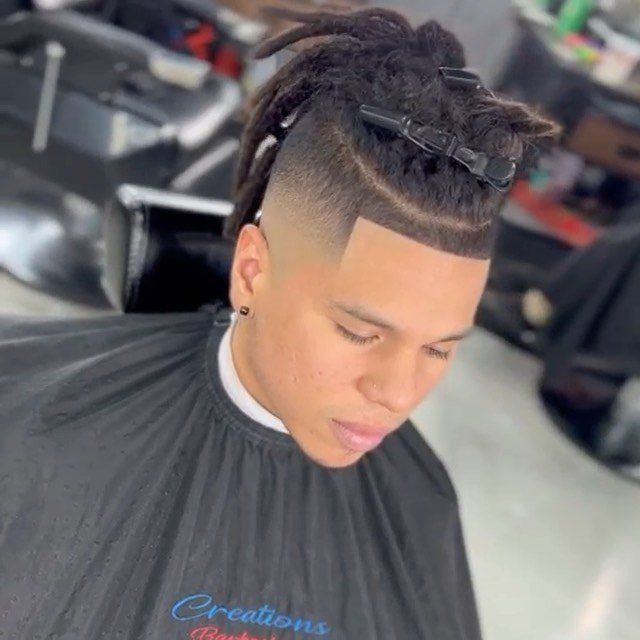 A man with dreadlocks is getting his hair cut at a barber shop.