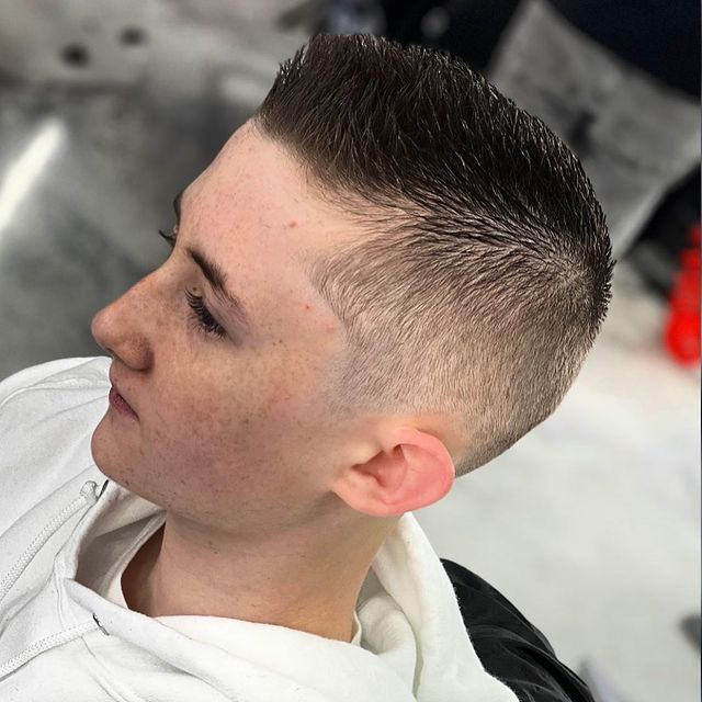 A young boy with a very short haircut is sitting in a chair.