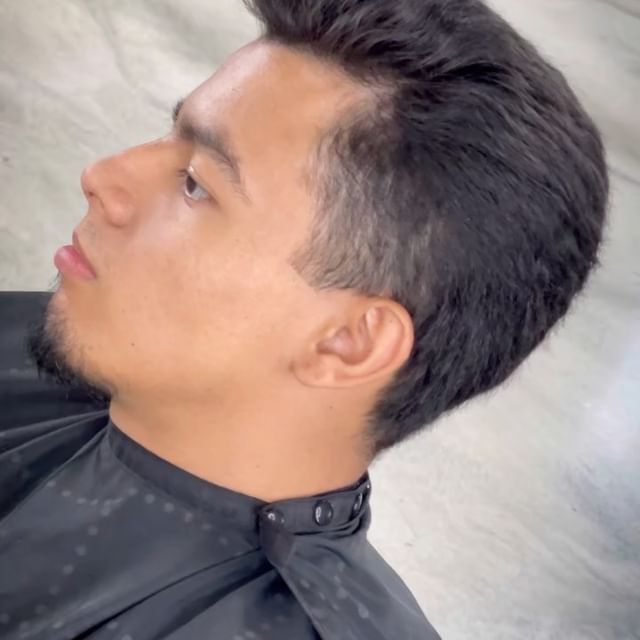 A man with a beard is sitting in a chair wearing a black cape.