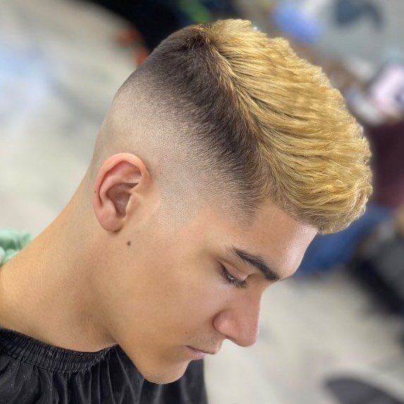 A young man with blonde hair is getting his hair cut by a barber.