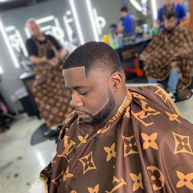 A man is getting his hair cut by a barber wearing a louis vuitton cape