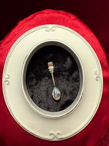 A decorative spoon inside a round white frame, set against a red velvet background.