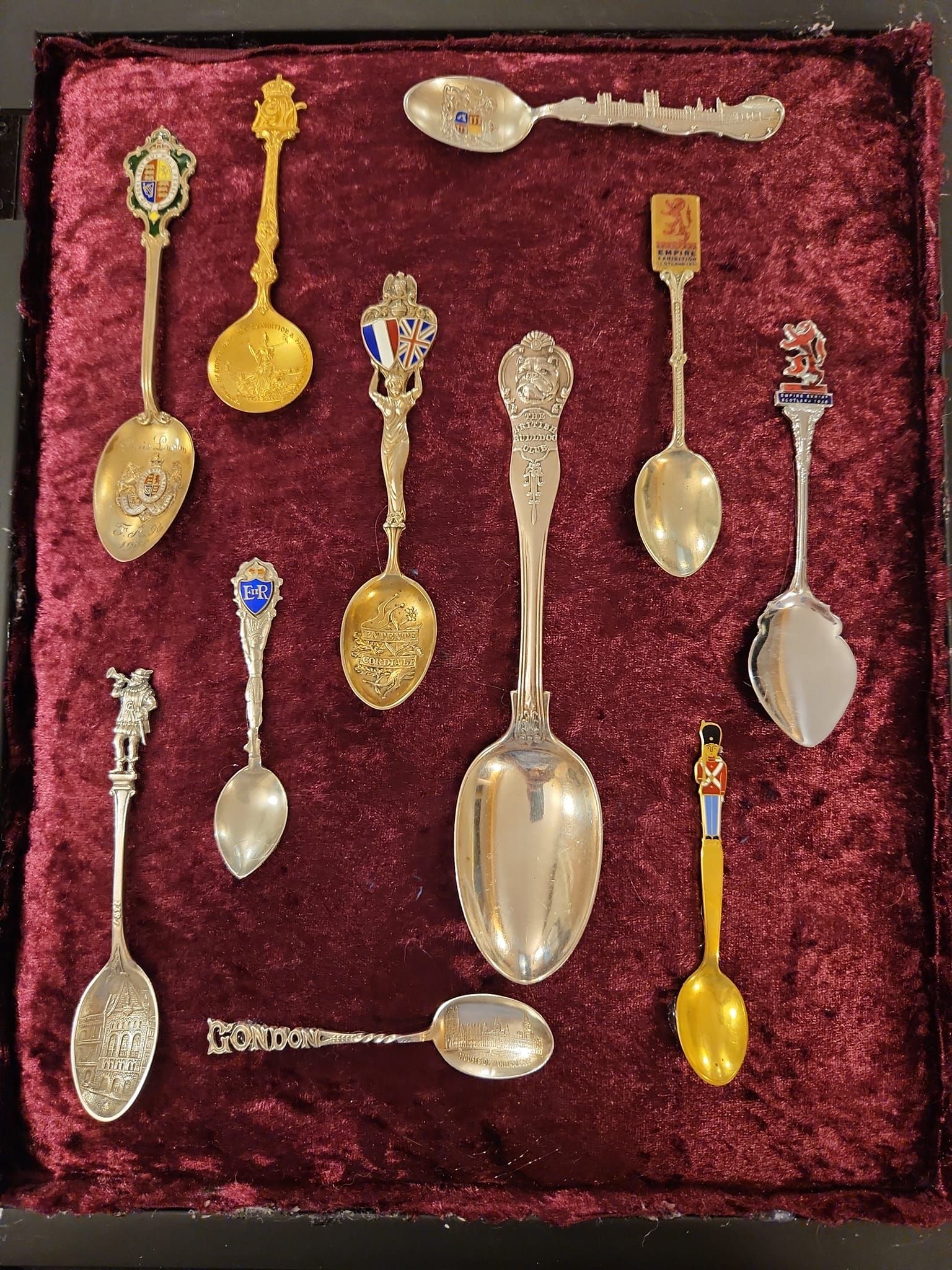 A collection of decorative spoons displayed on a dark red velvet surface.