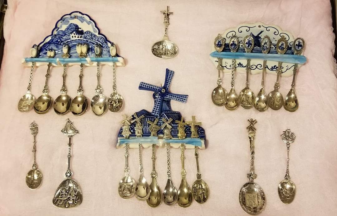 Collection of Dutch Delftware and silver spoons displayed on pink fabric.