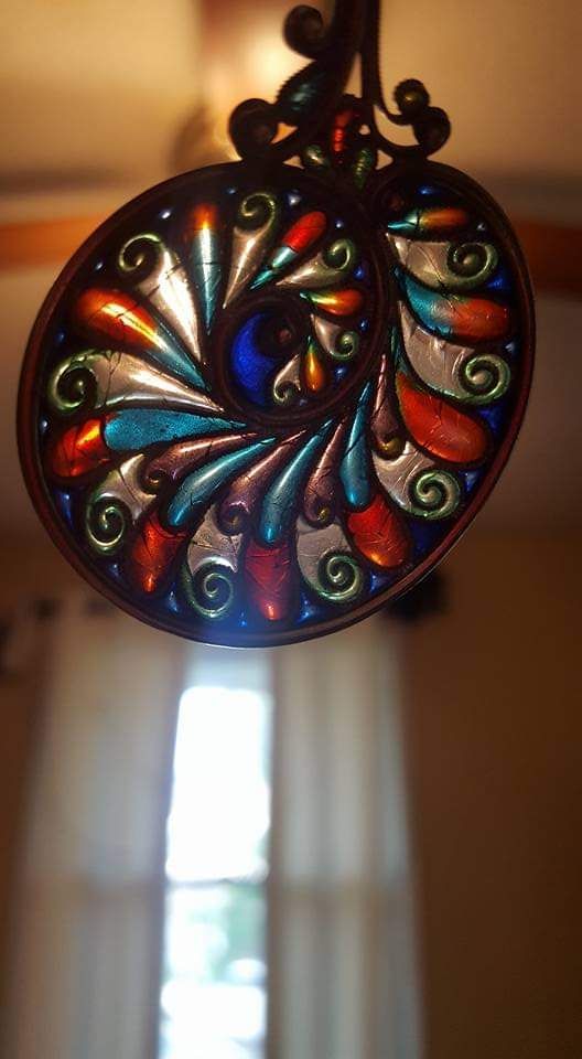 Stained glass nautilus shape, vibrant colors, hanging in front of a window.
