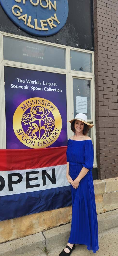 Woman in blue dress and hat stands.