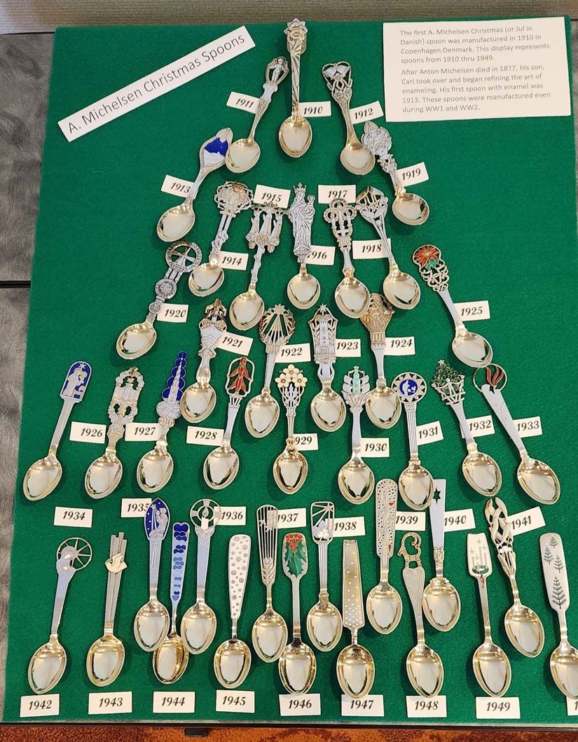 Display of antique silver spoons arranged on a green background.