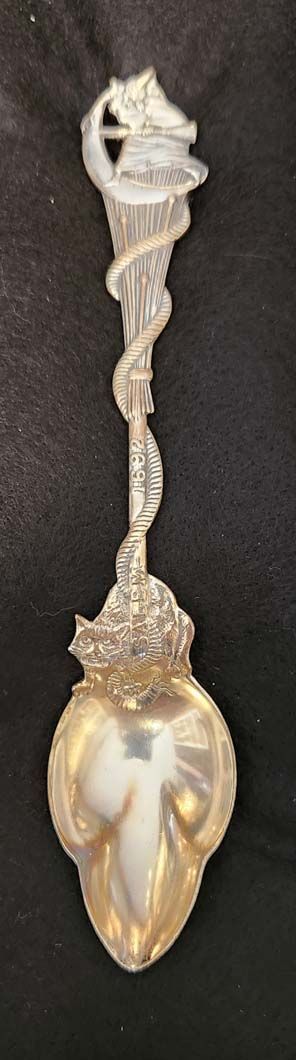 Silver spoon with ornate, swirling handle and detailed bowl, set against a dark background.