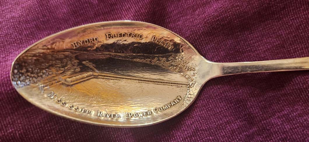 Silver spoon with etched scene and text on a purple surface.