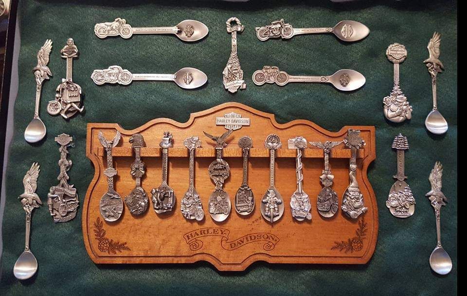 Collection of souvenir spoons displayed on a wooden plaque and green fabric background.