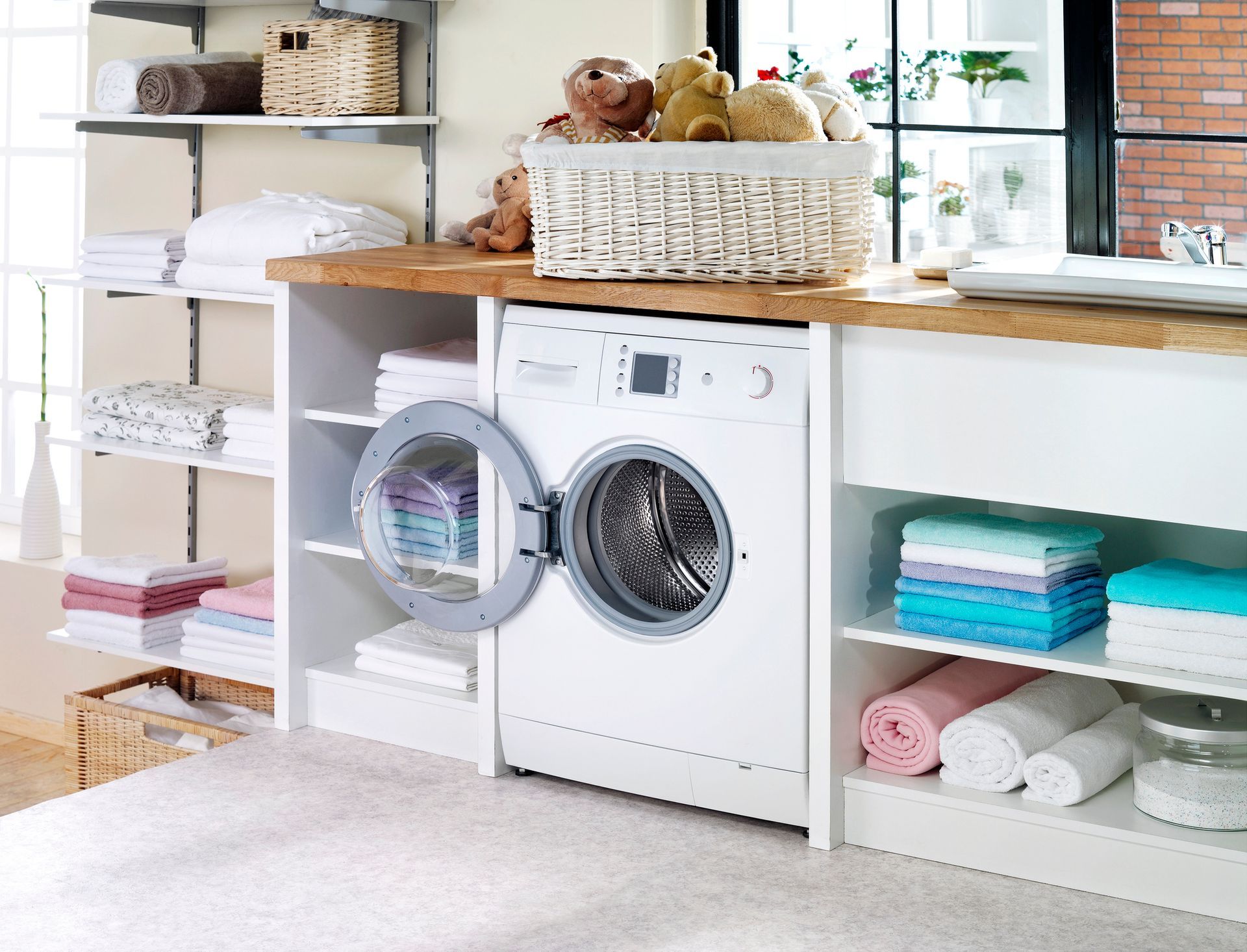 A laundry room with a washing machine and a basket of teddy bears