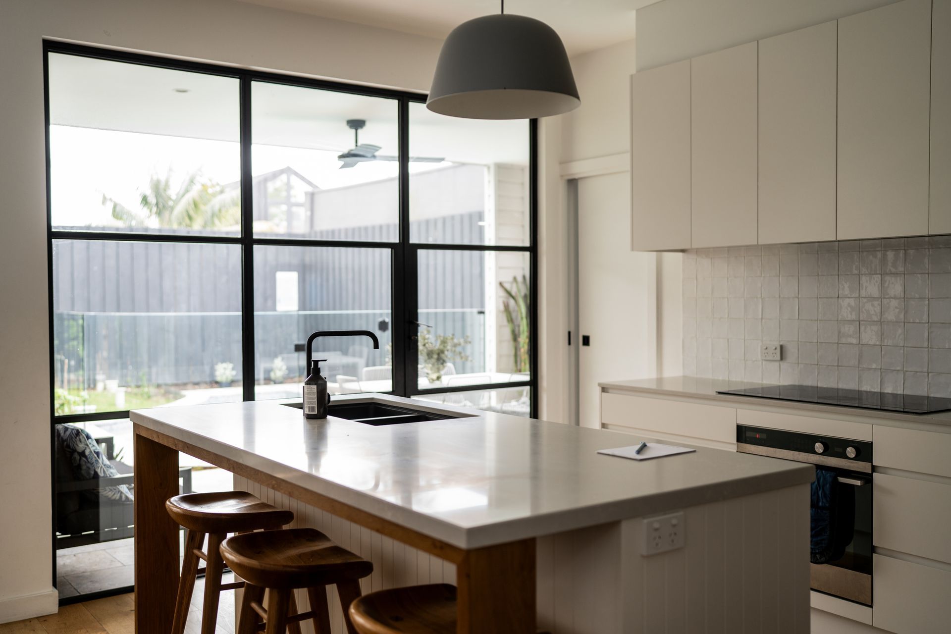 A kitchen with a large island and stools and a large window.