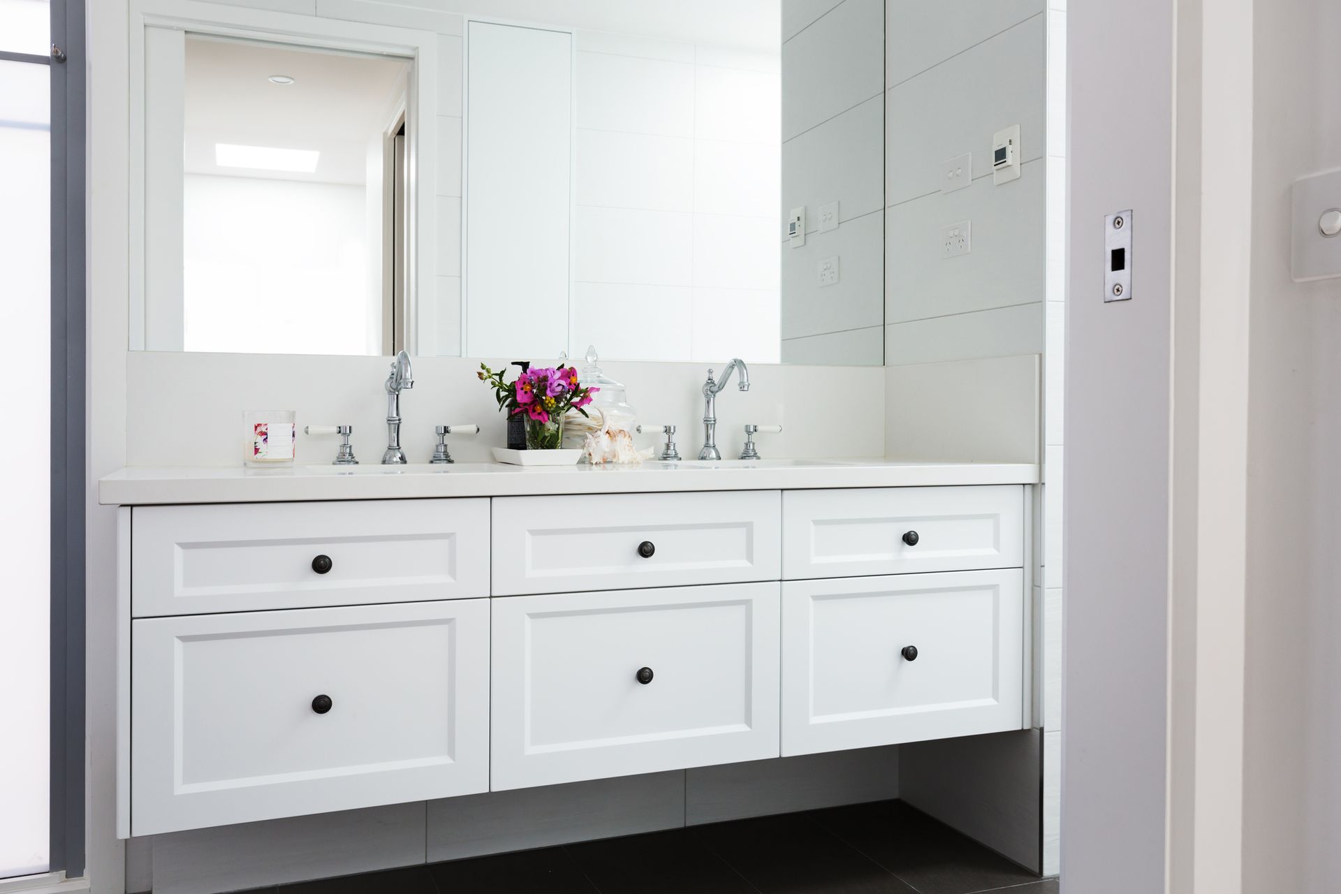 A bathroom with two sinks , a mirror and white cabinets.